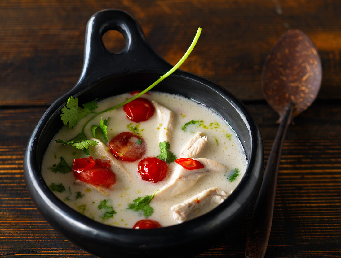 Pot of Thai chicken soup with coconut milk and cherry tomatoes