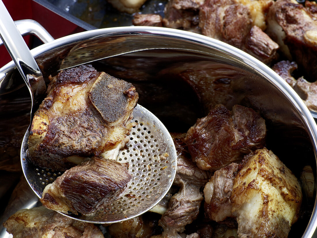 Close-up of roasted dark beef on ladle for preparation of beef stock, step 3