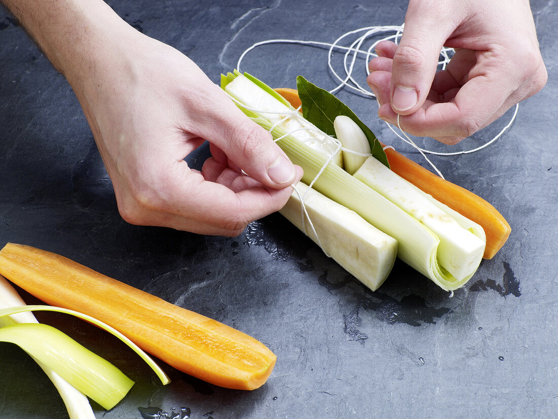 Close-up of hand tying vegetables for preparation of beef stock, step 5