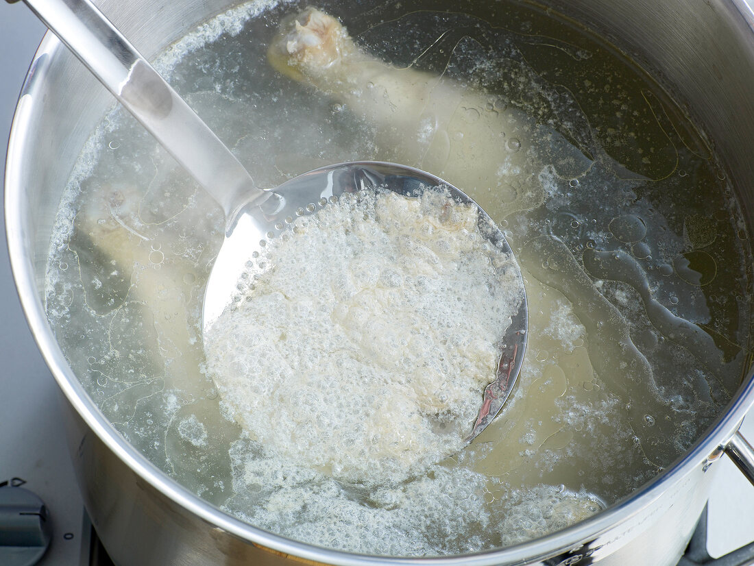 Removing froth with ladle from pan for preparation of chicken stock, step 3