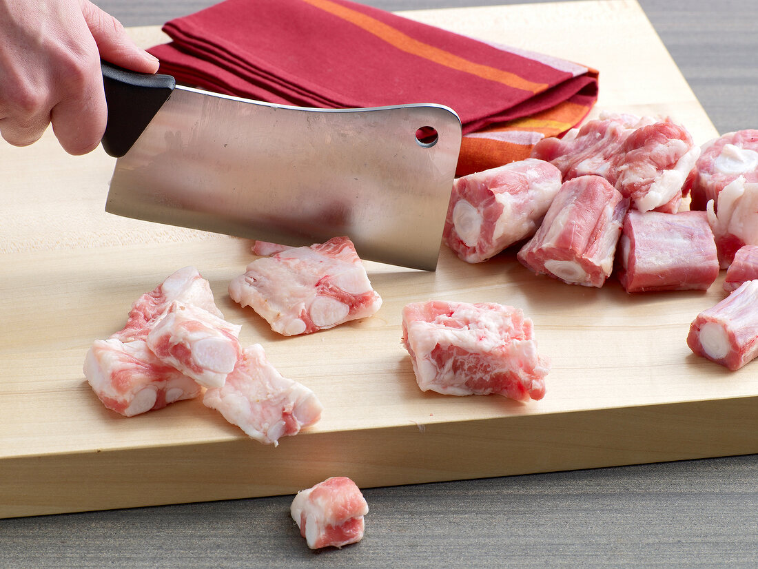 Cutting veal pieces on wooden board for preparation of veal stock, step 1