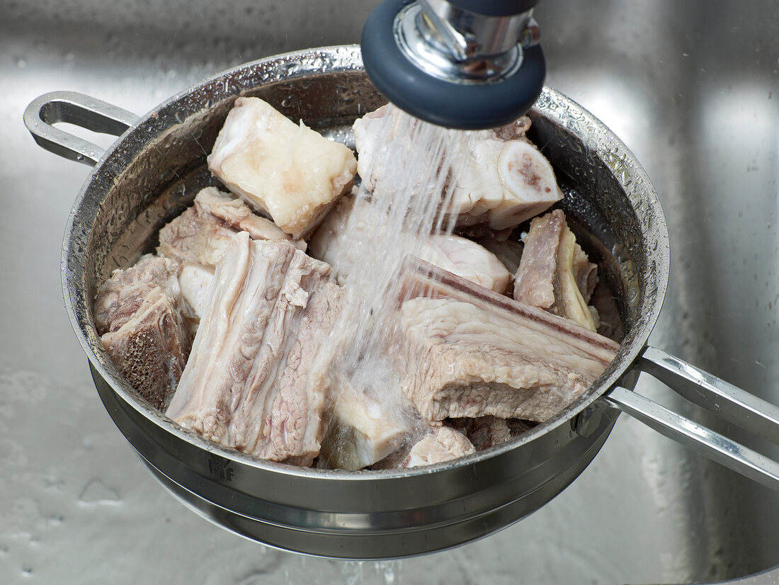 Close-up of beef pieces being washed with water for preparation of beef stock, step 2