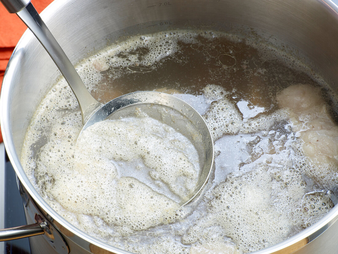 Close-up of froth being removed with sieve for preparation of beef stock, step 4