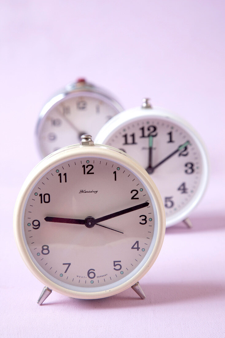 Close-up of three clocks against pink background