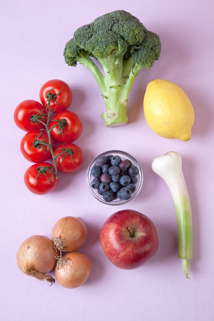 Broccoli, tomatoes, lemon, garlic, onions, apples and blueberries on pink background