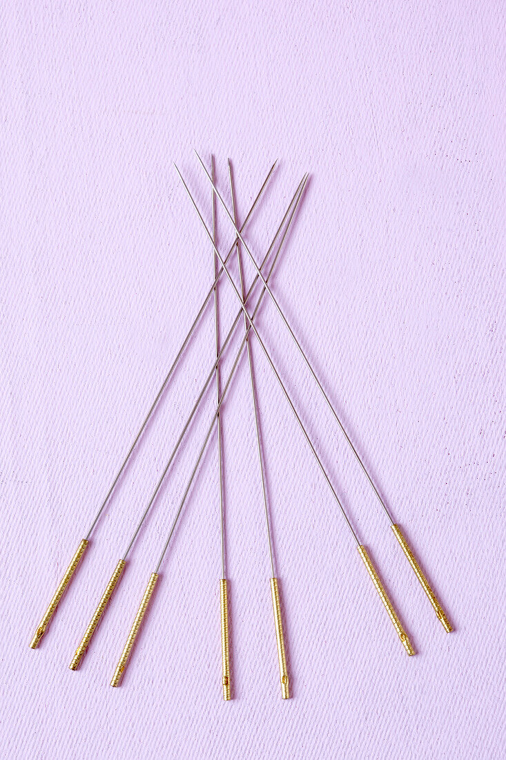 Close-up of acupuncture needles on purple background, overhead view