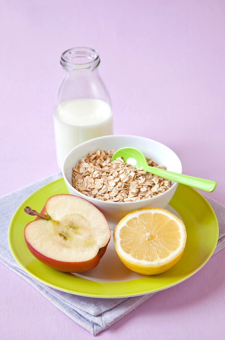 Bottle of milk, oats in bowl, halved apple and orange on wooden platter