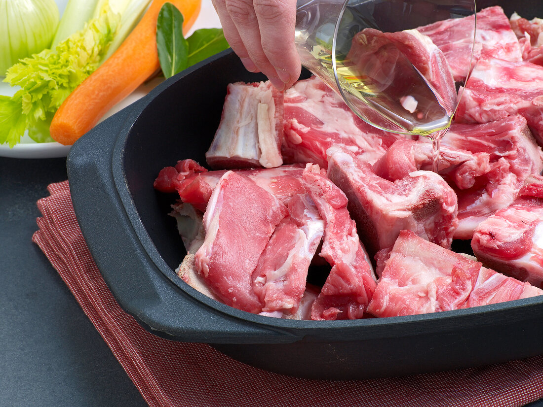 Oil being poured on veal pieces in baking tray for preparation of demi glace veal, step 1