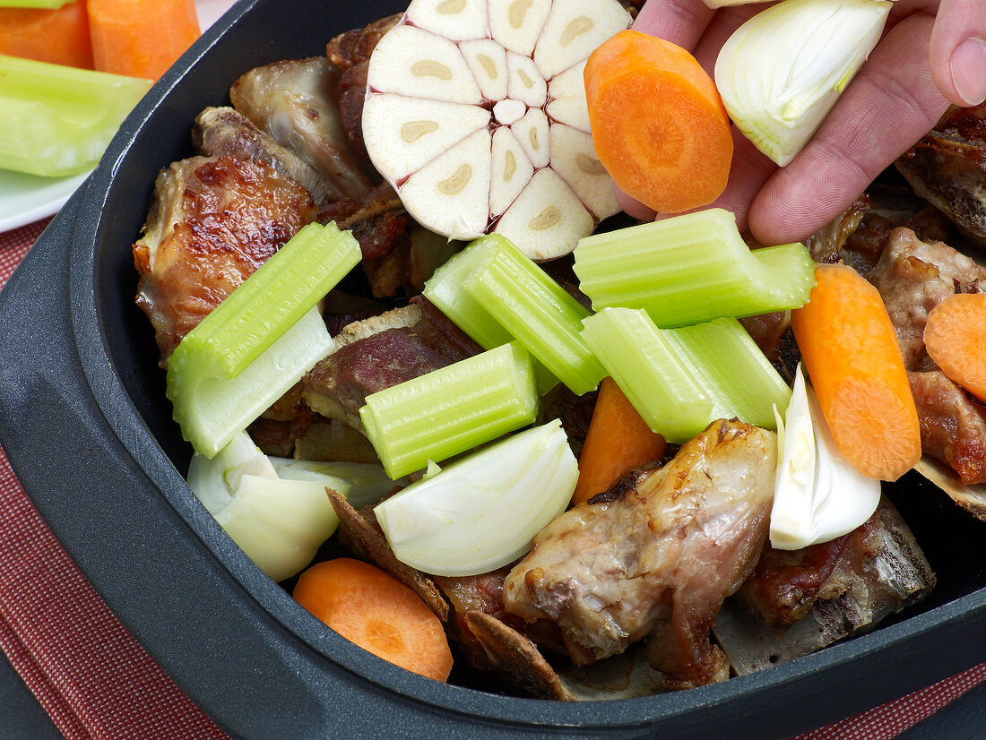 Fresh vegetables being added on roasted veal for preparation of demi glace veal, step 2