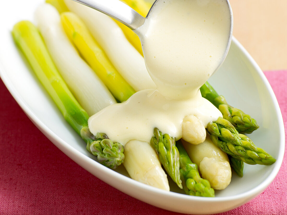 Close-up of hollandaise sauce being poured on asparagus in serving dish 