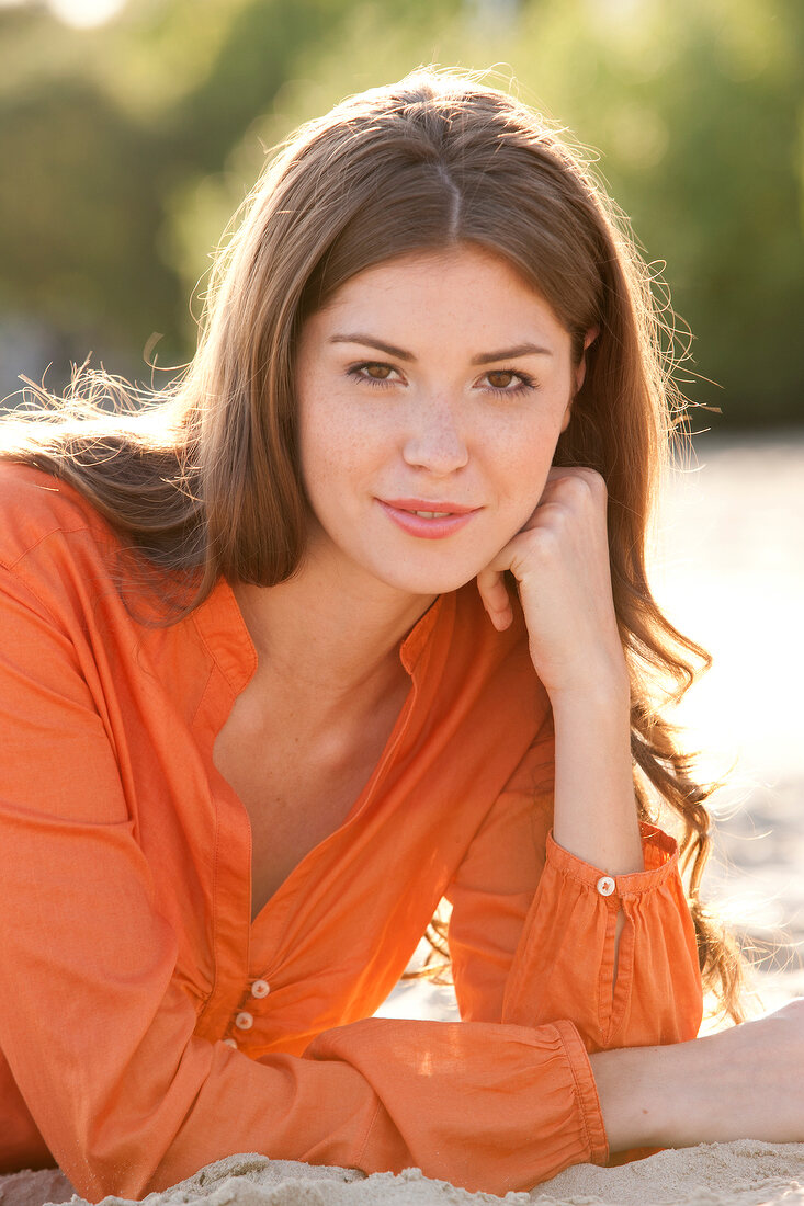 Portrait of pretty brunette woman wearing orange blouse with hand on checks, smiling