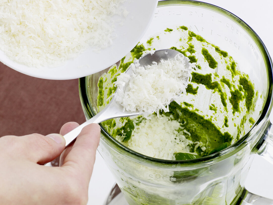 Close-up of grated pecorino cheese being added to pesto in grinder, step 2