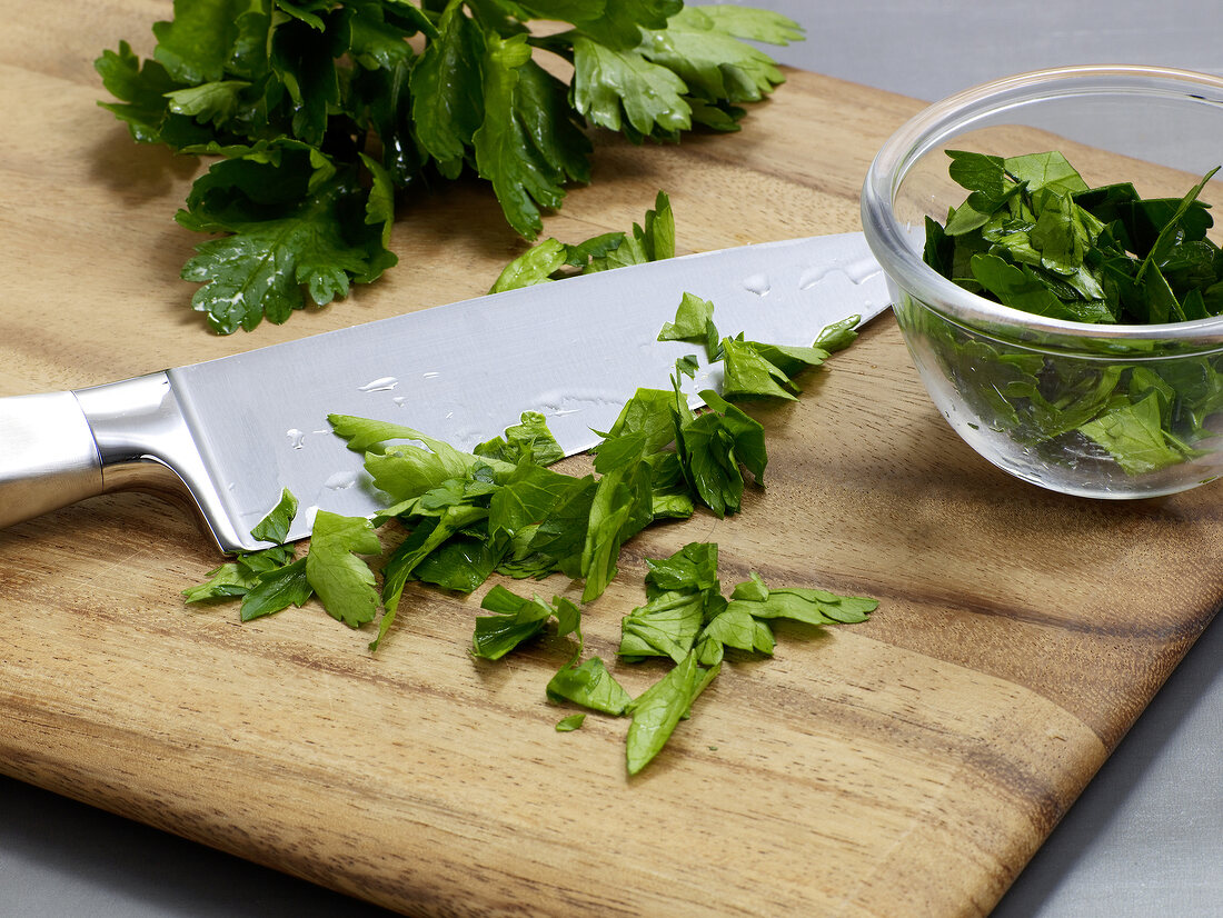 Parsley leaves being chopped on wooden board for preparation of salsa verde, step 1