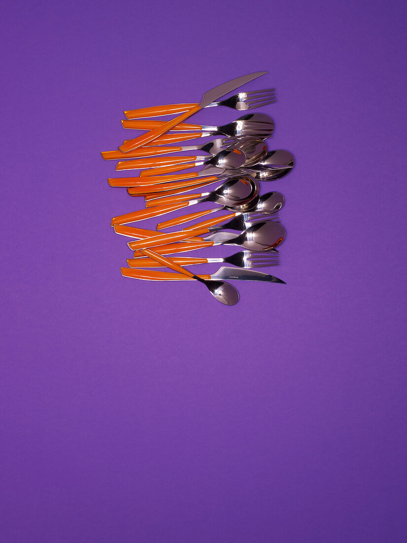 Stainless steel cutlery with red plastic handles on purple background