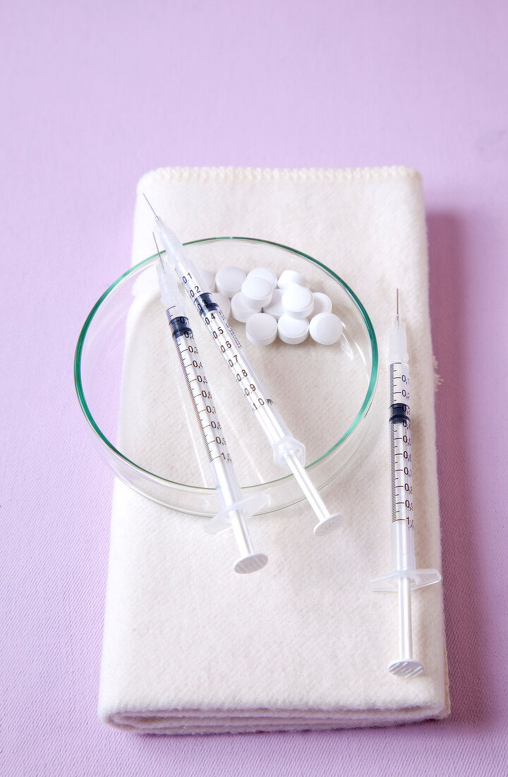 Close-up of three syringes and tablets kept in bowl and white napkin