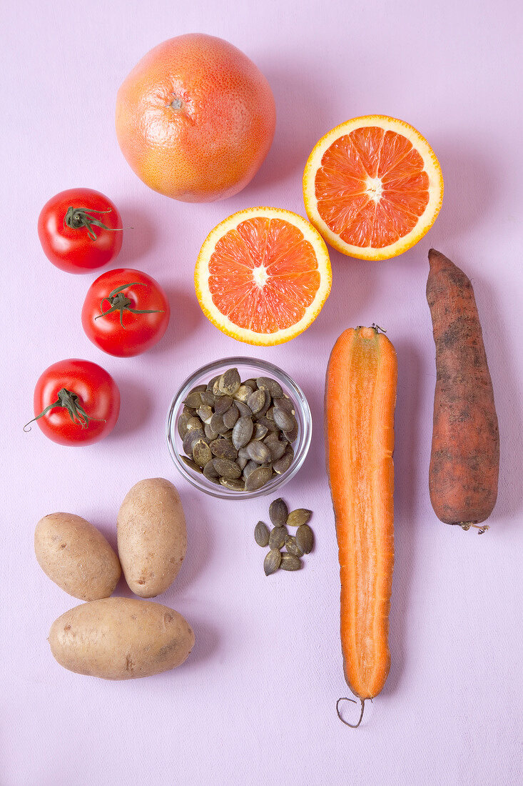 Halved oranges, carrots, tomatoes, potatoes and seeds on pink background