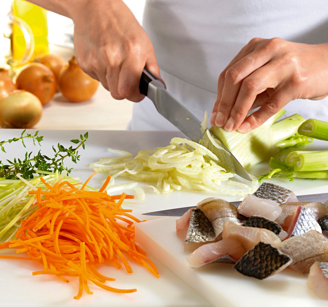 Close-up of hand chopping fennel beside chopped carrot and fillet