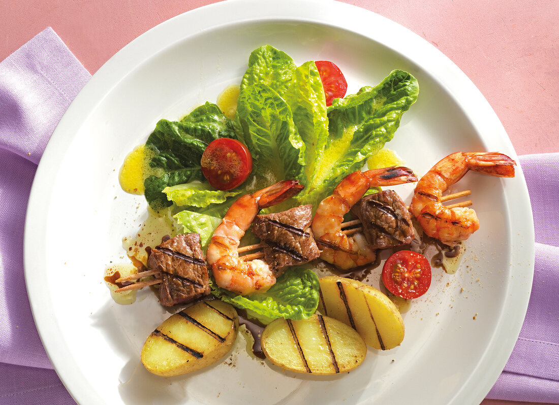 Close-up of salad with shrimp and steaks in skewers on plate