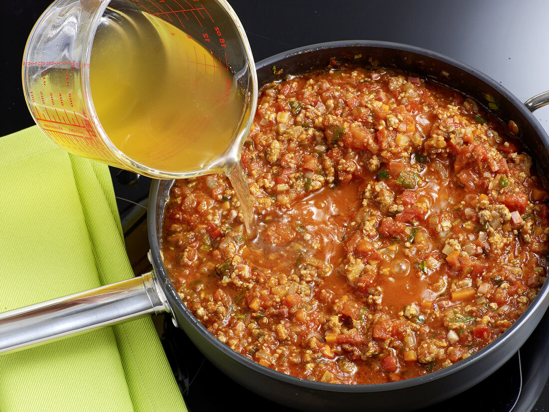 Close-up of olive oil being poured in Bolognese sauce, step 7