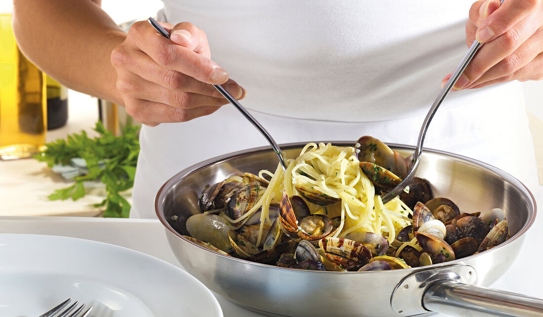 Close-up of hand mixing spaghetti and clams in pan for preparation of spaghetti vongole