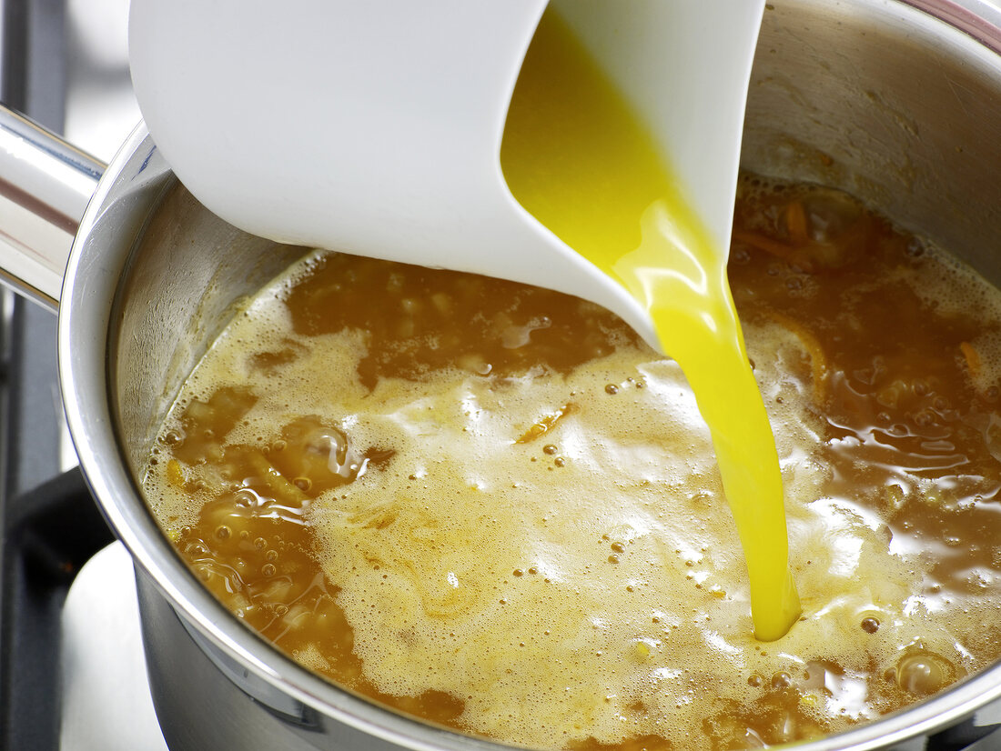 Close-up of lemon juice being poured to orange sauce in sauce pan