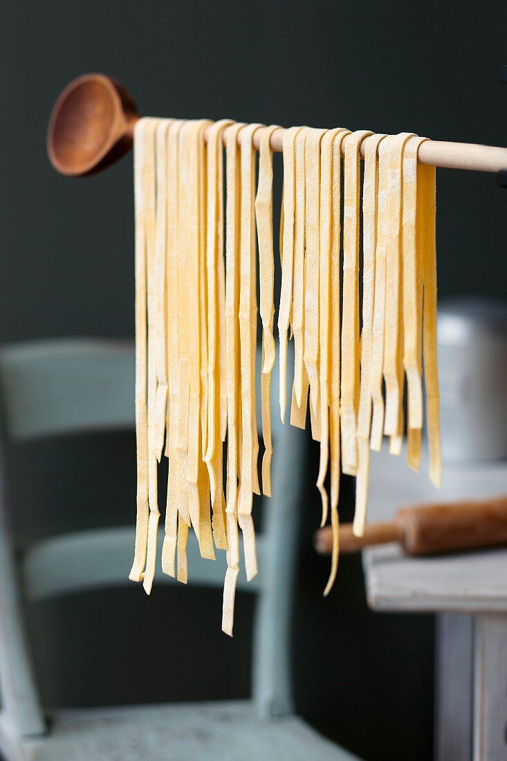 Fresh tagliatelle hanging from a wooden spoon to dry