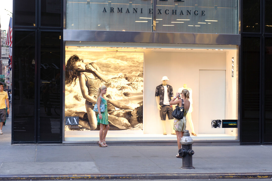 Woman photographing other woman in front of Advertisement on 5th Avenue, New York