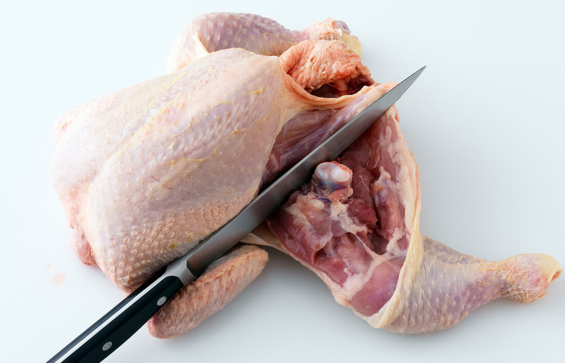Close-up of leg of chicken being chopped on white background, step 2