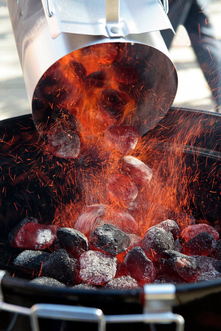 Brennende Holzkohle wird in einen Grill geschüttet