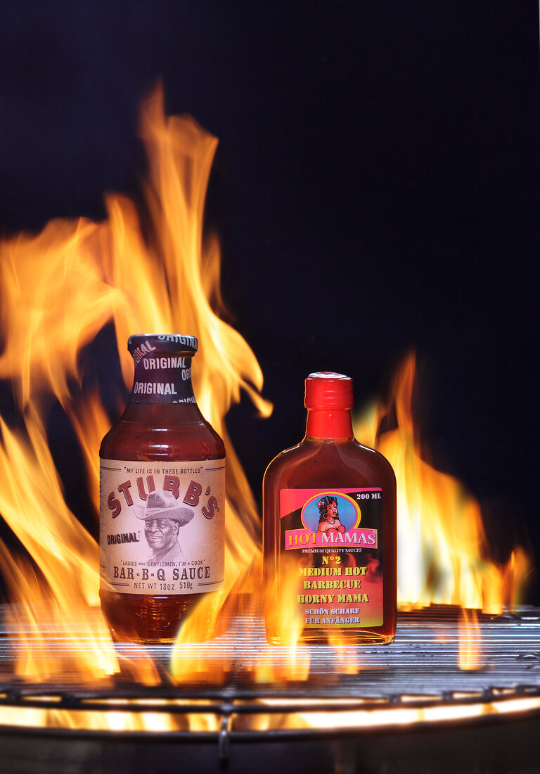 Two different barbecue sauces on grill with flames