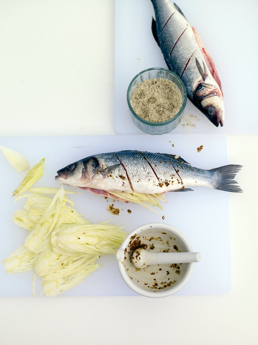 Two sea bass sprinkled with fennel and salt on chopping board