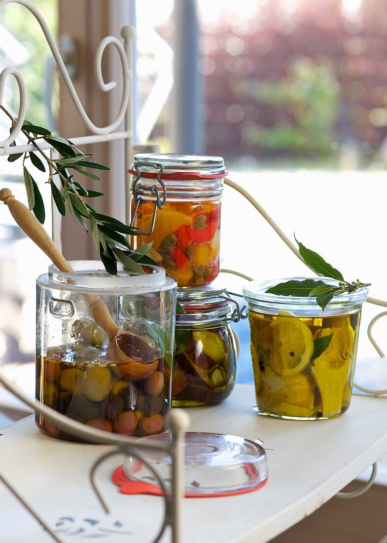 Vegetables preserved in oil in preserving jars on a table by a window