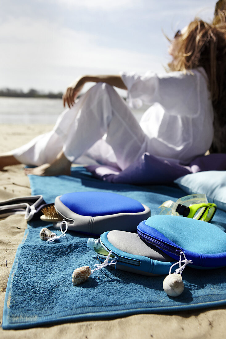 Toiletry bags on towel in front of woman sitting on beach