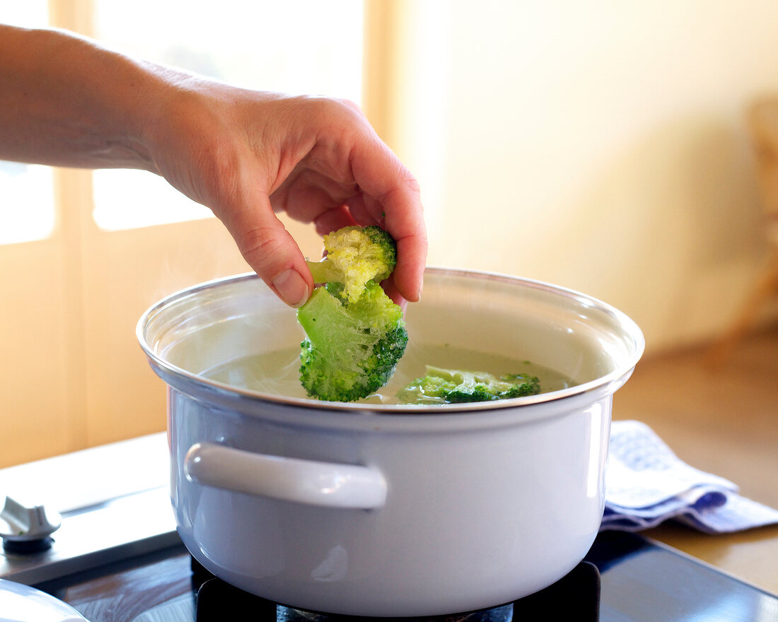 Close-up of hand adding broccoli in hot water