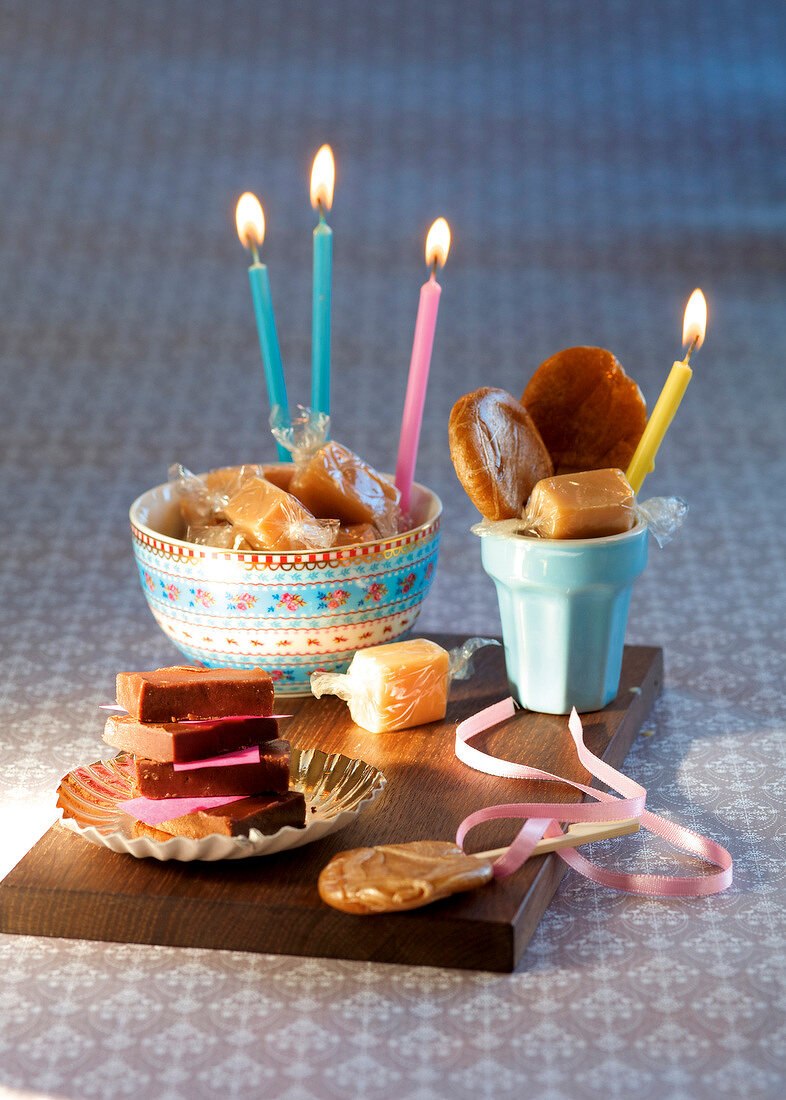 Homemade caramel, toffees and lollipop with lit candles on wooden board