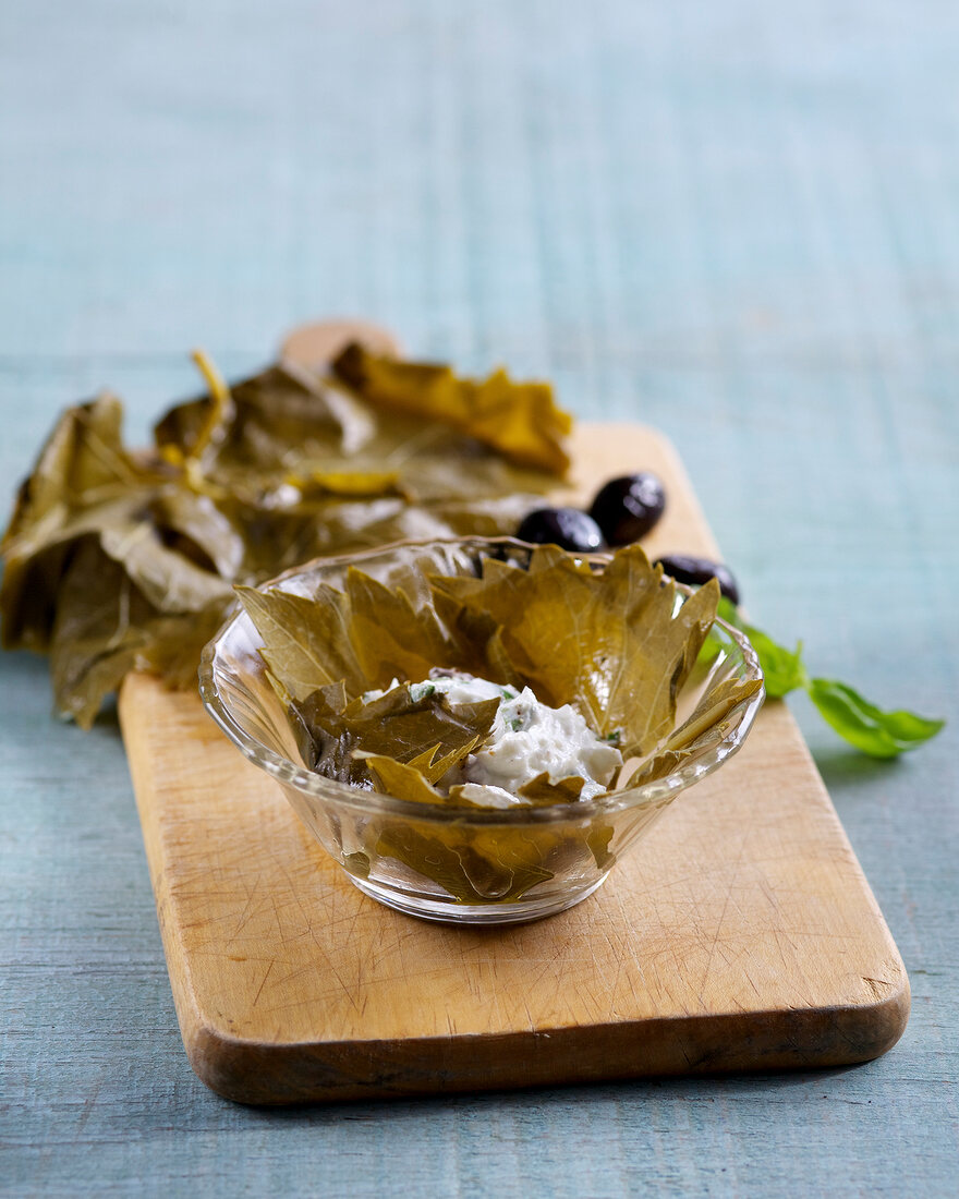 Goat cheese wrapped with vine leaves in bowl on wooden board