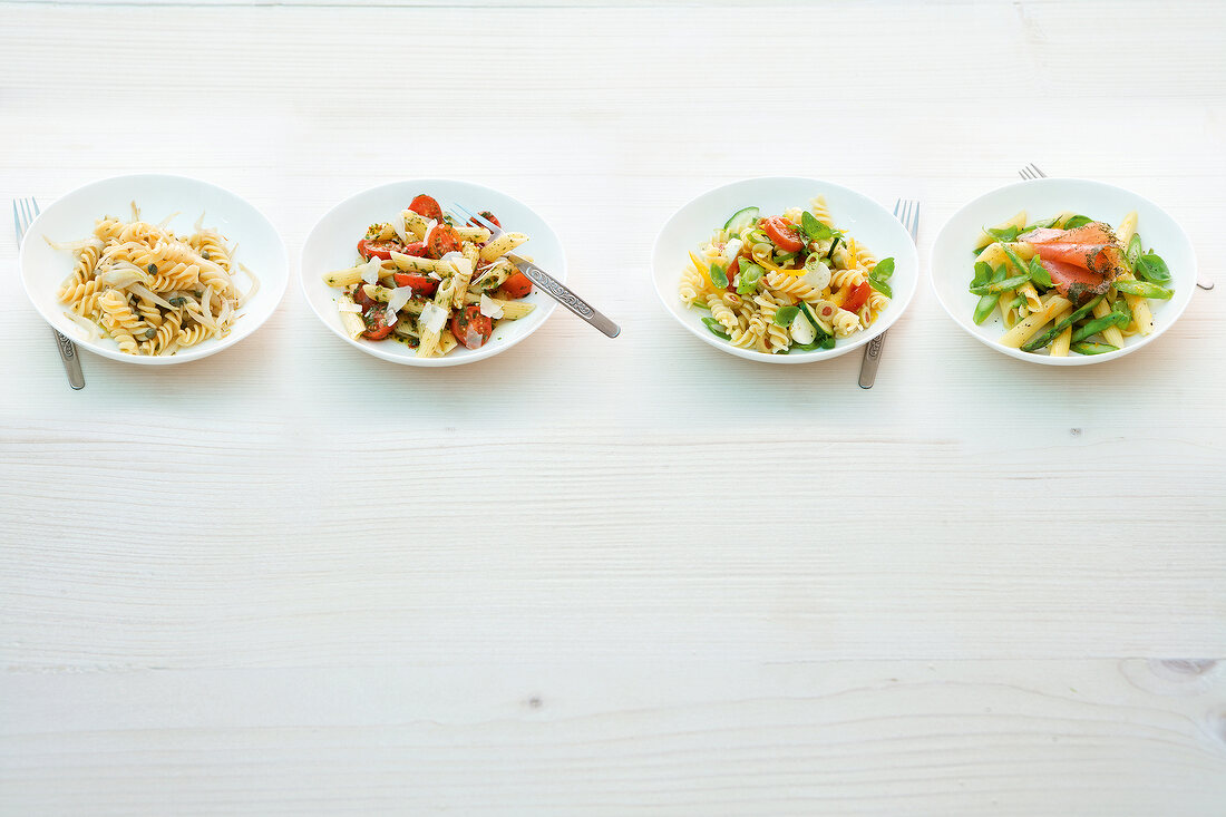 Four plates with different types of pasta salads on white background