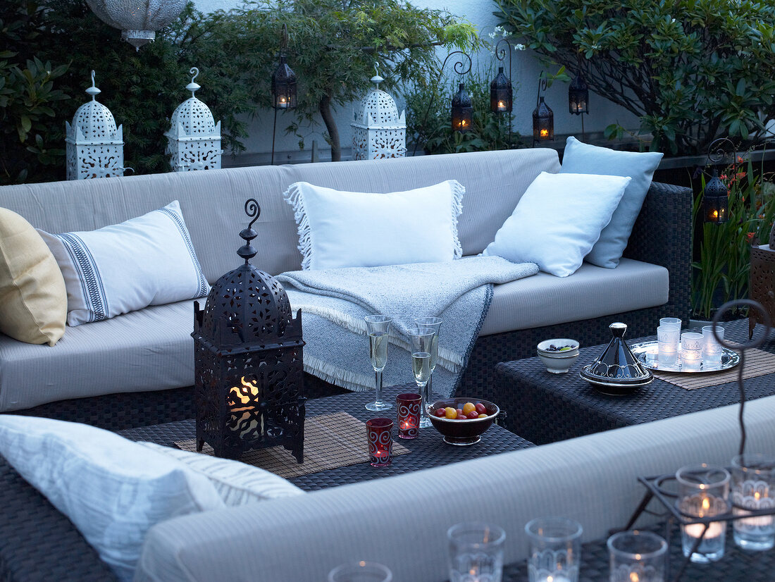 Sofa, cushion and lit candles arranged outdoors at evening