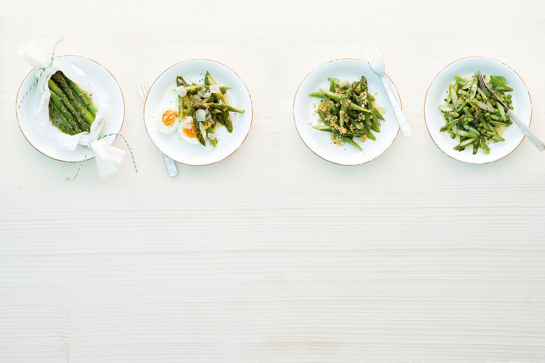 Four different dishes of green asparagus on plates