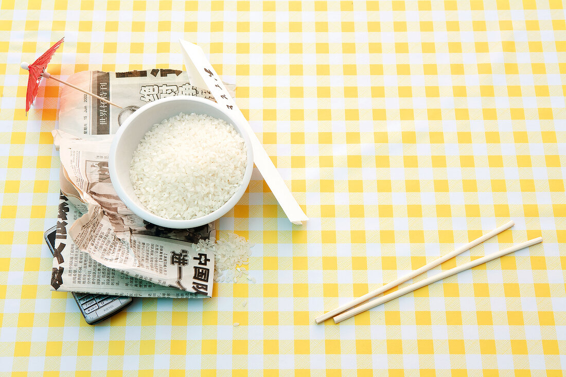 Bowl with rice, Asian newspaper and chopsticks on yellow checked cloth