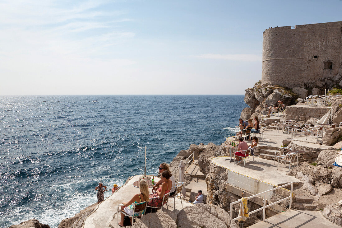 People sitting on rock near sea in Dubrovnik, Croatia