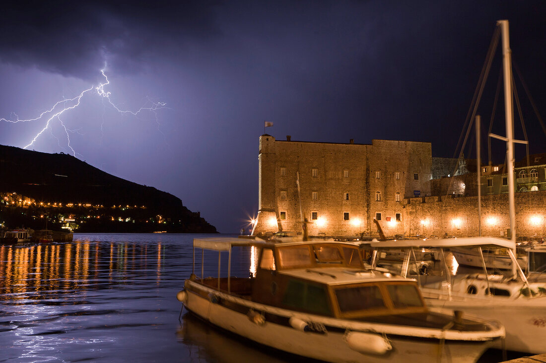 Boats moored on Dubrovnik old harbour with thunderstorm at night in Croatia