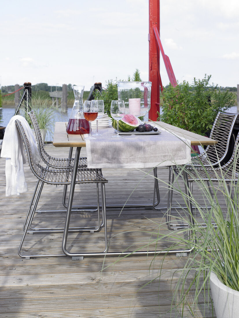 Table with dishes, chairs on terrace near water