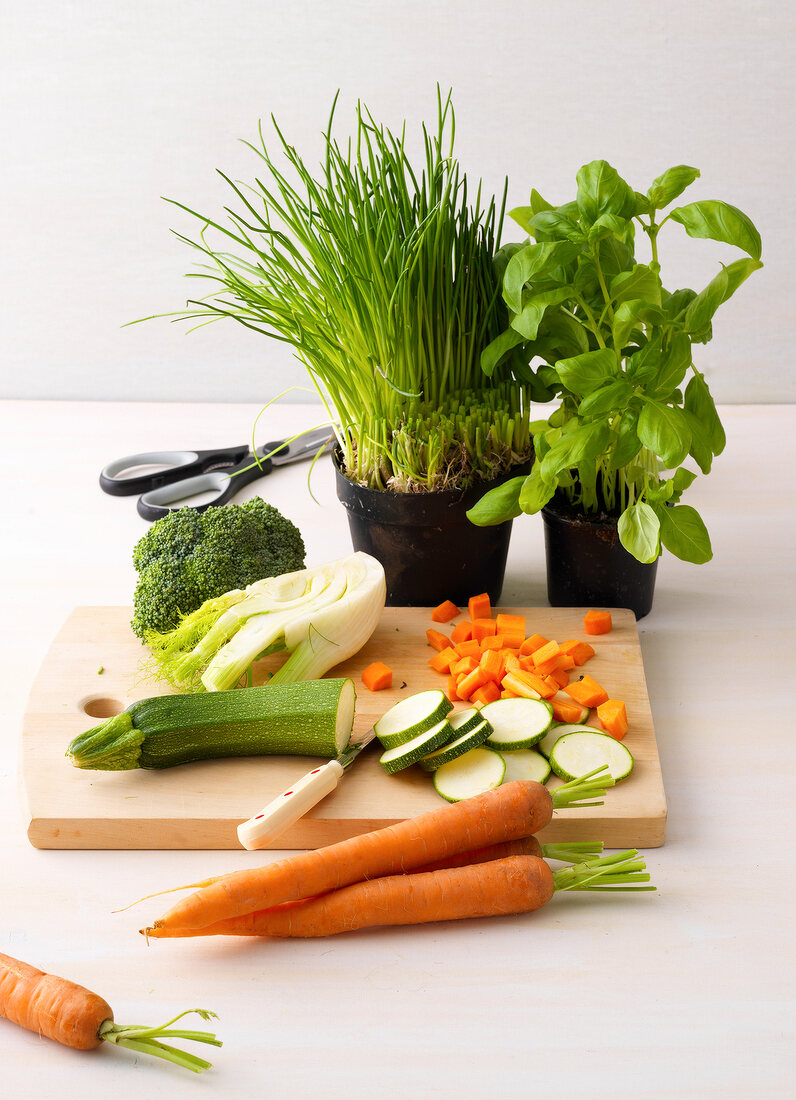 Whole and sliced fresh vegetables on chopping board and herbs