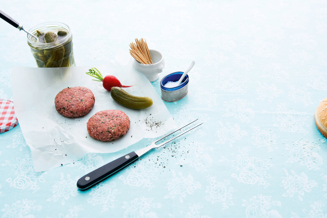 Two raw burgers with cucumbers and radishes on white background