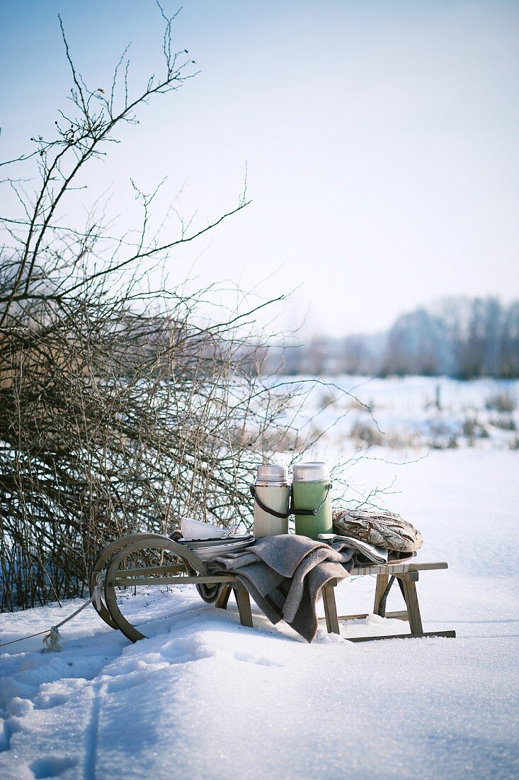 Schlitten mit Decke und Thermoskannen in winterlicher Landschaft