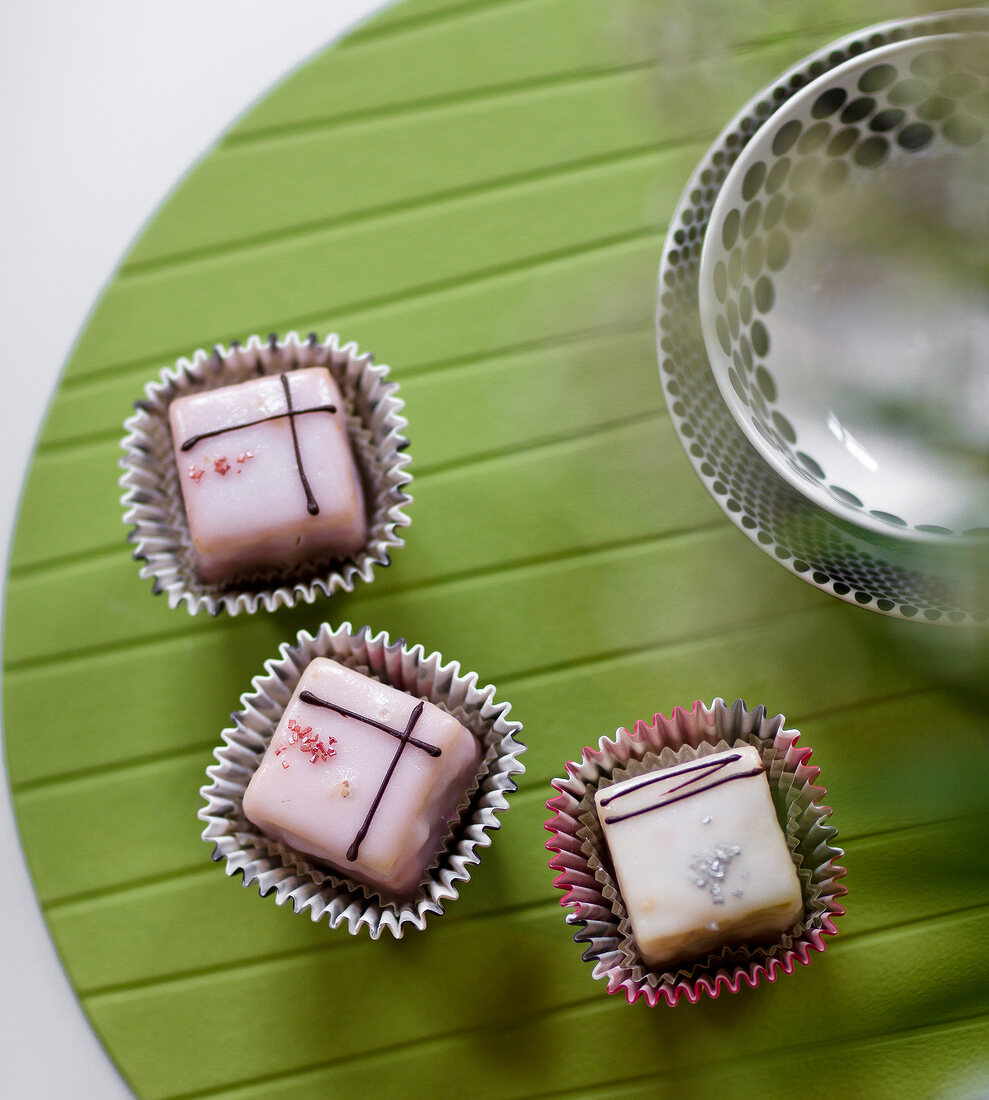 Three chocolate sweets in paper cases on green base