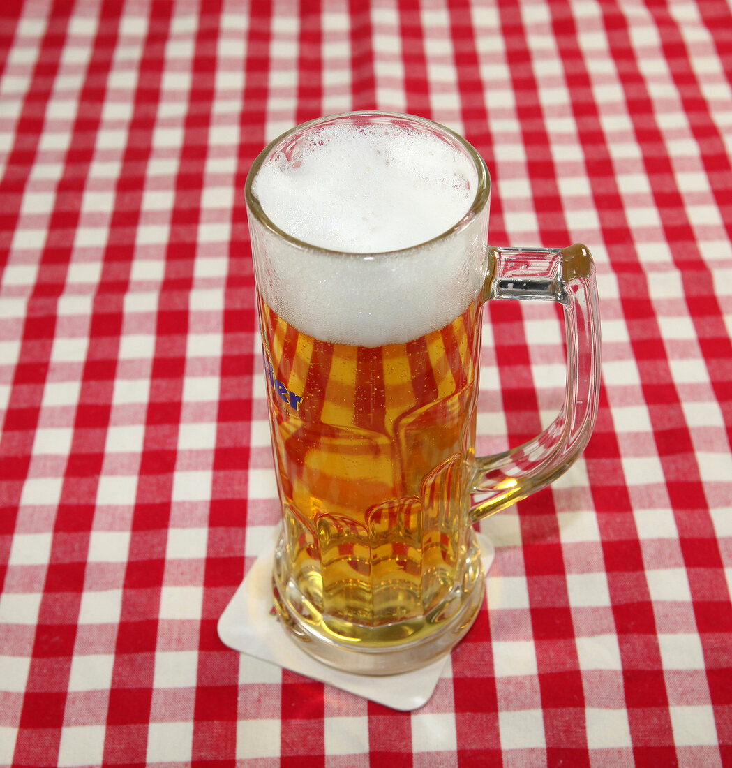 Bier in großem Glas mit Henkel steht auf Tischdecke.