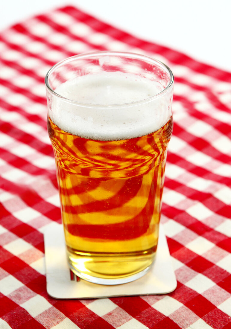 Bier in Glas mit wenig Schaum steht auf Tischdecke.