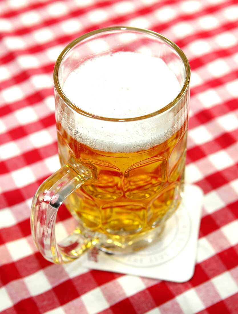 Bier in kleinem Glas auf Bierdeckel und rot-weiß karierter Tischdecke